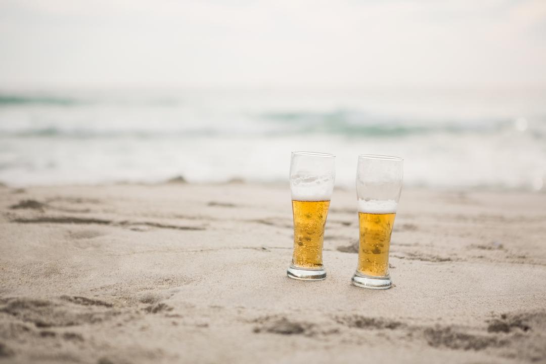 Two Beer Glasses on Sandy Beach with Ocean in Background - Free Images, Stock Photos and Pictures on Pikwizard.com
