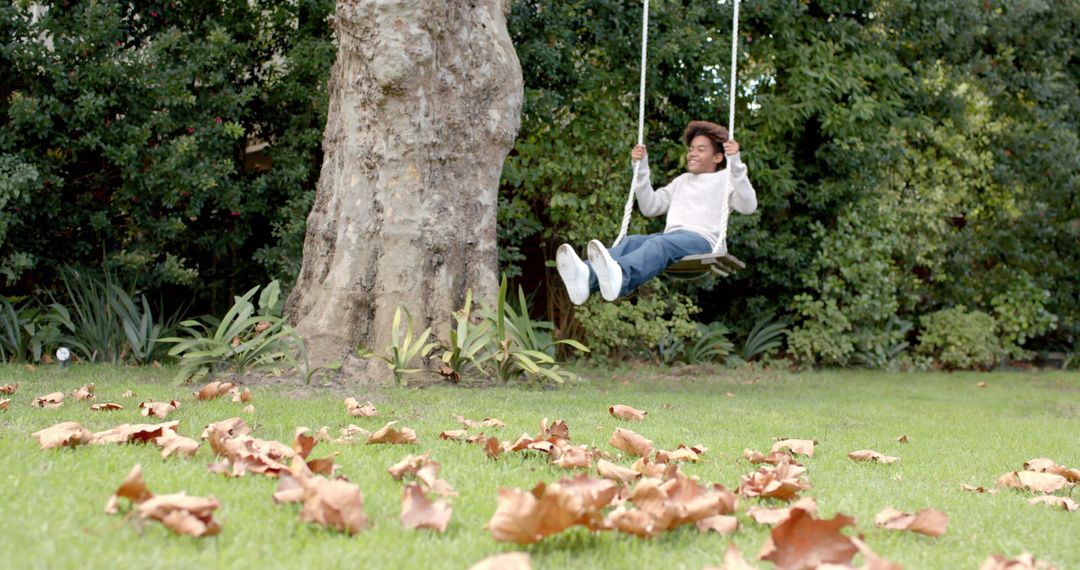 Joyful African American Boy Swinging on Tree in Autumn Garden