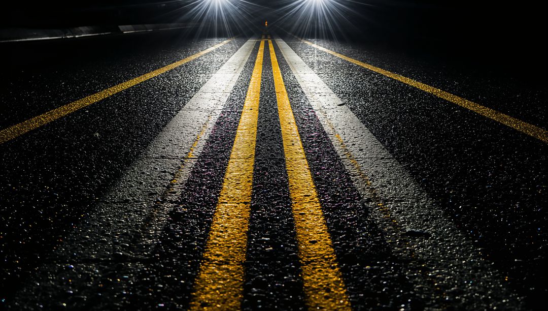 Glowing double yellow centerline reflecting under headlights on wet asphalt at night