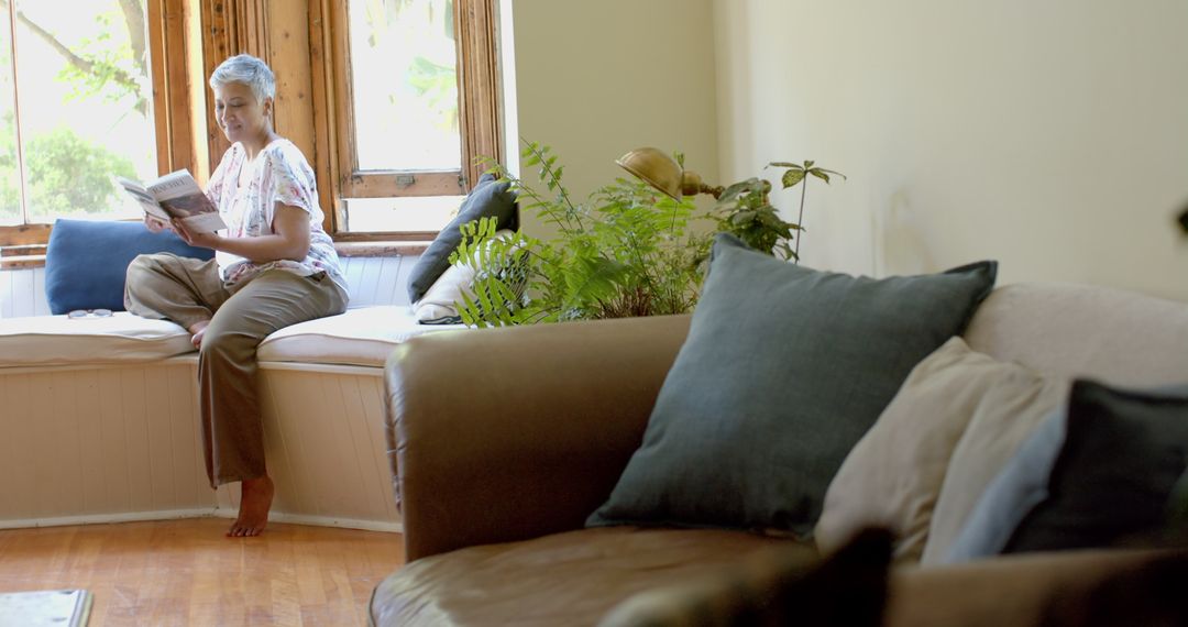 Senior Woman Reading by Window with Comfortable Couch at Home
