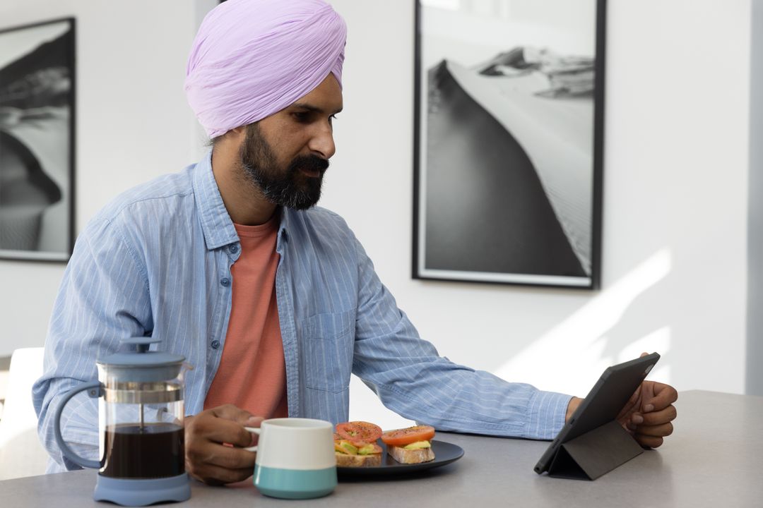 Man with Turban Using Tablet Sipping Coffee Modern Kitchen