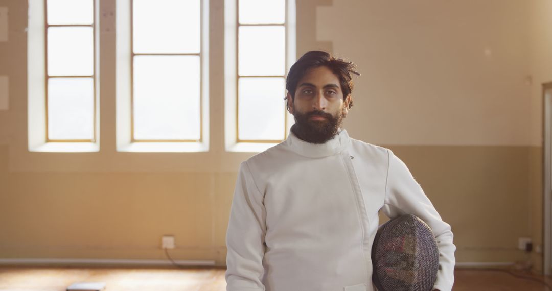 Confident Fencer Standing with Helmet in Sunlit Room