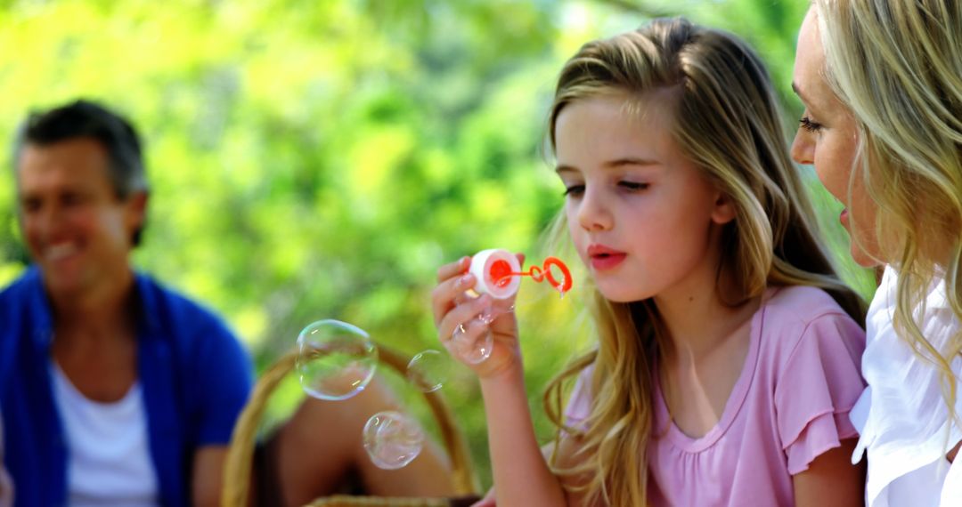 Young Girl Blowing Bubbles Outdoors with Family - Free Images, Stock Photos and Pictures on Pikwizard.com