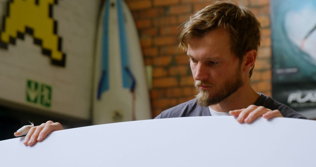 Man Inspecting Surfboard with Brick Wall in Background - Free Images, Stock Photos and Pictures on Pikwizard.com