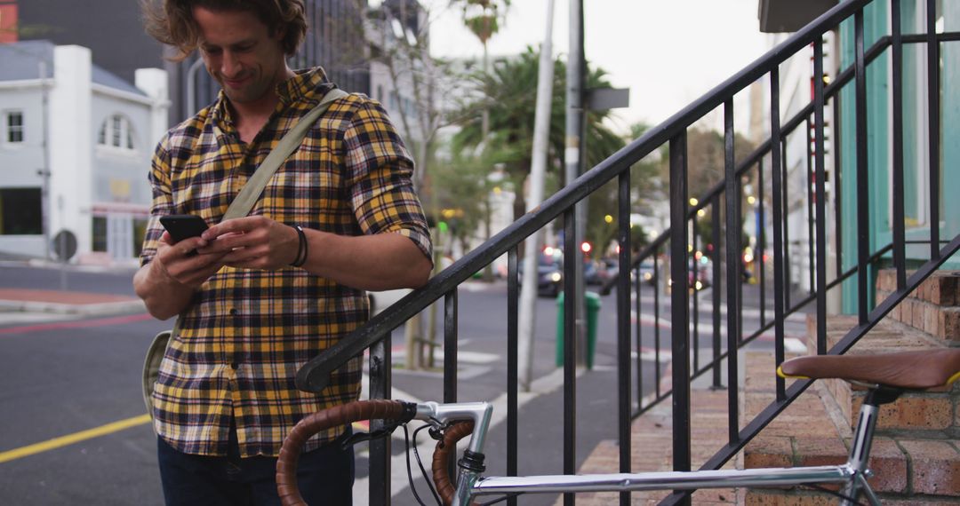 Man using smartphone while leaning on railing near bicycle in city - Free Images, Stock Photos and Pictures on Pikwizard.com