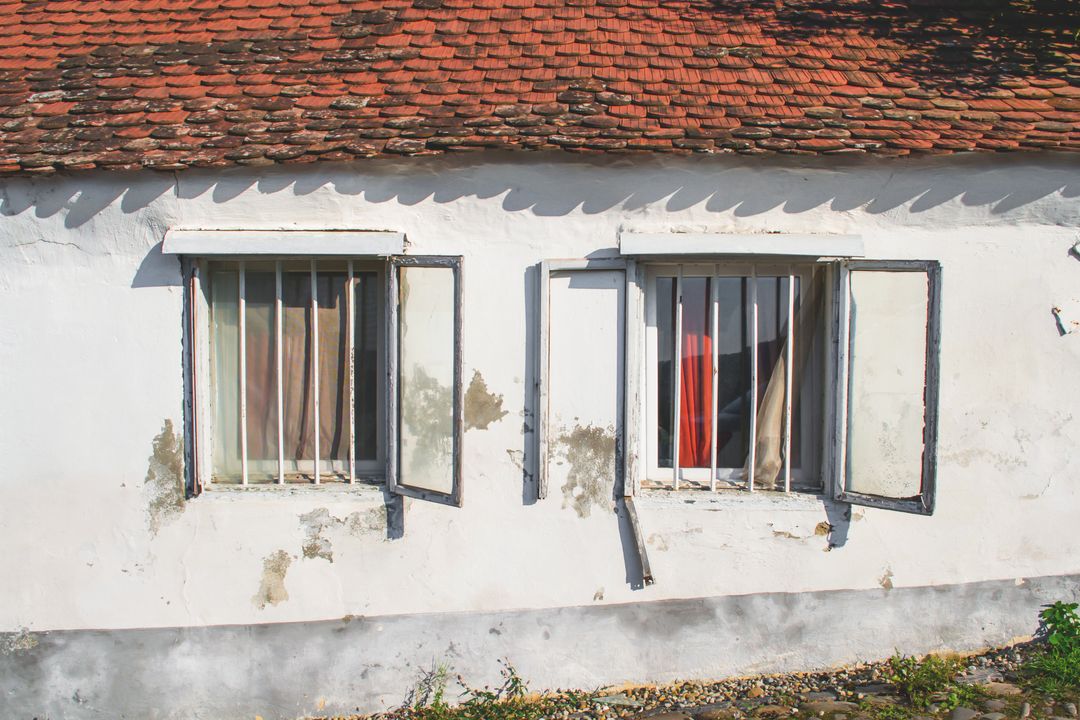 Aged White Cottage Wall Featuring Open Shutter Windows under Red Tiled Roof, Peeling Plaster