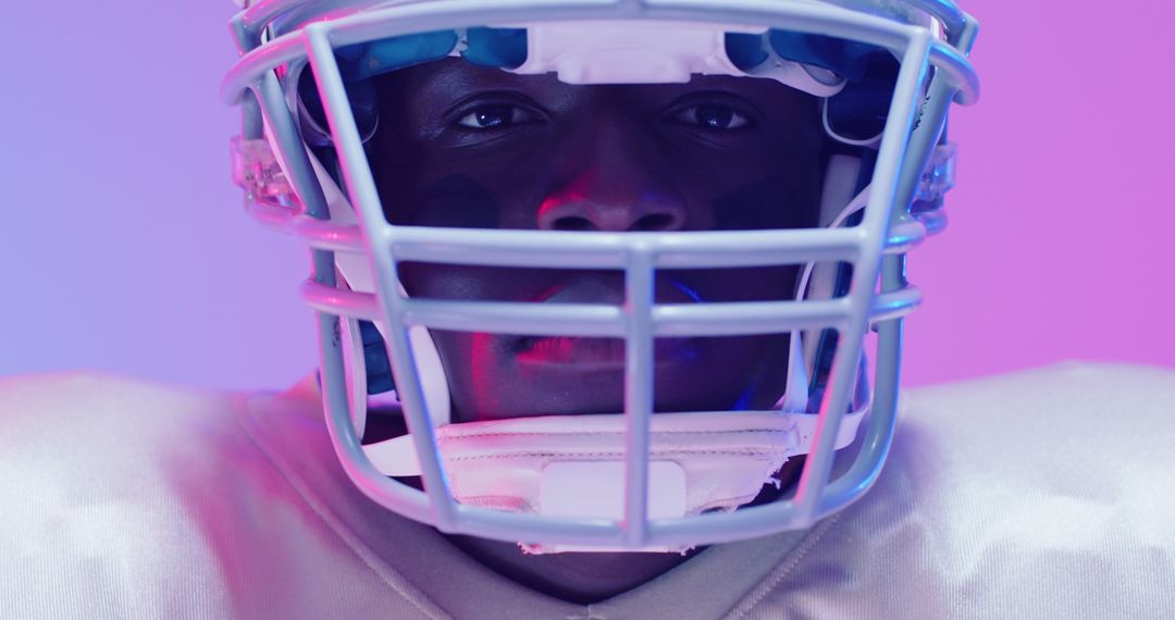 Focused African American Football Player with Helmet Under Blue and Pink Lighting - Free Images, Stock Photos and Pictures on Pikwizard.com