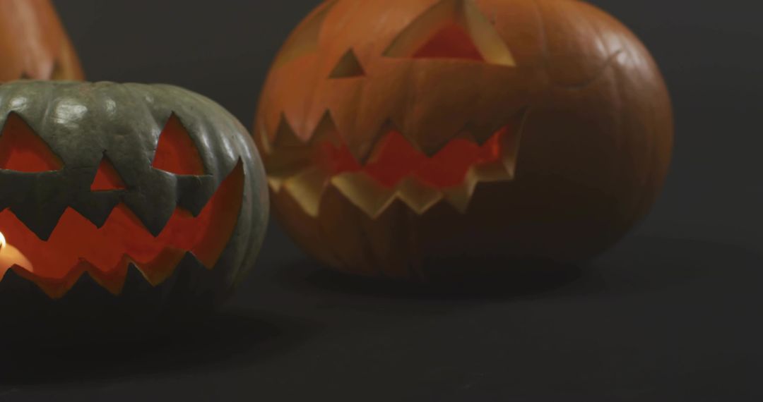 Glowing carved jack-o'-lantern duo casting warm candlelight on black background still life