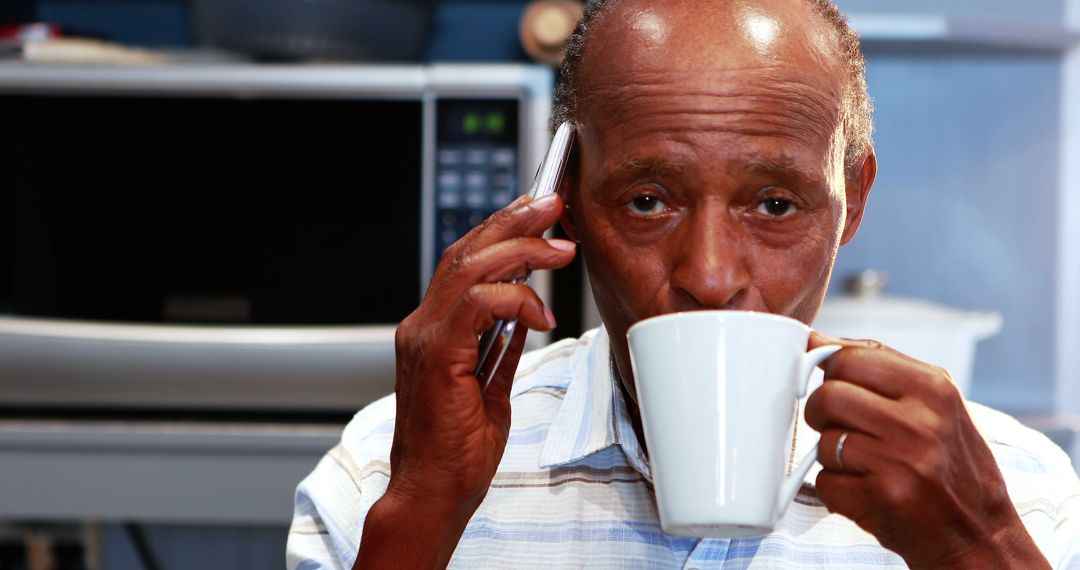 Older man drinking coffee and talking on phone in kitchen - Free Images, Stock Photos and Pictures on Pikwizard.com