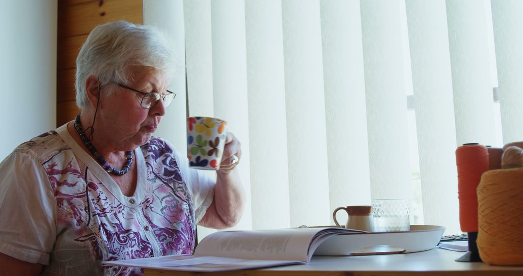 Senior woman reading and drinking coffee by window - Free Images, Stock Photos and Pictures on Pikwizard.com