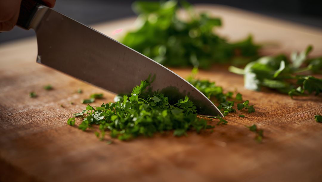 Sharp Chef's Knife Chopping Fresh Herbs on Wooden Board