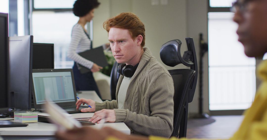 Focused Redhead Man Working at Office Desk with Colleagues Around - Free Images, Stock Photos and Pictures on Pikwizard.com