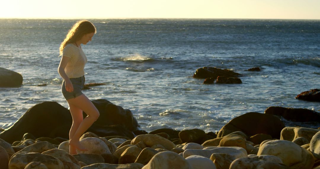 Young Woman Walking On Rocky Beach At Sunset - Free Images, Stock Photos and Pictures on Pikwizard.com