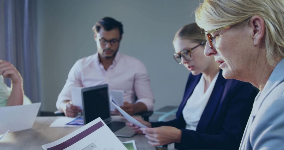 Senior professional reading documents during focused business meeting with diverse team