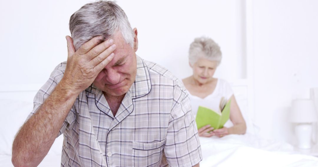 Elderly Man with Headache Sitting on Bed, Partner Reading Behind - Free Images, Stock Photos and Pictures on Pikwizard.com