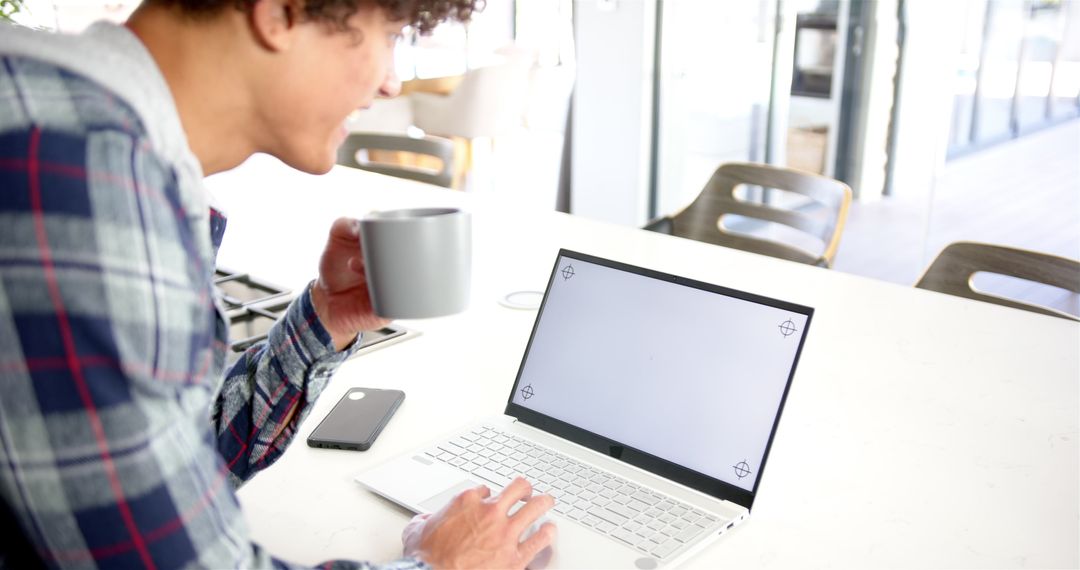 Man Holding Coffee Mug while Using Laptop in Modern Kitchen