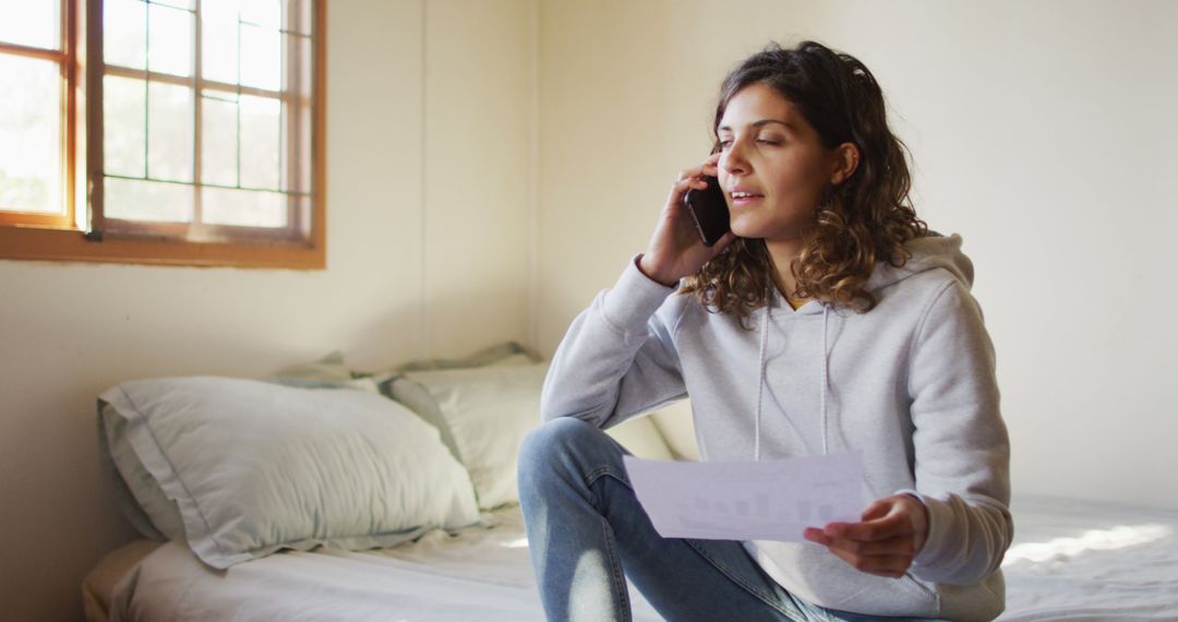 Young Woman Discussing Financial Document on Phone in Cozy Bedroom - Free Images, Stock Photos and Pictures on Pikwizard.com