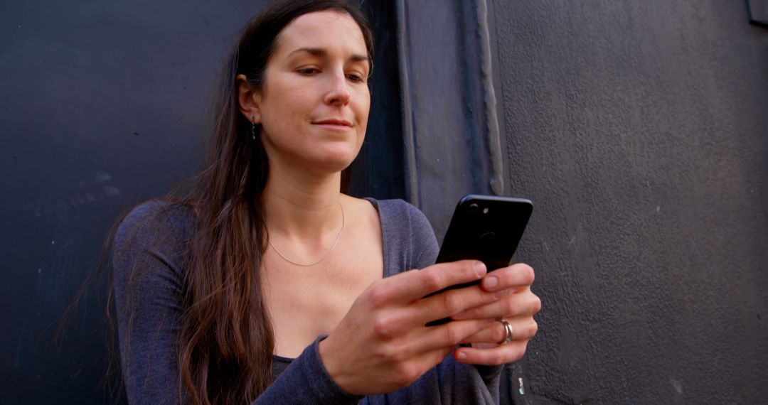 Woman with Long Hair Using Smartphone Outdoors Against Dark Grey Wall - Free Images, Stock Photos and Pictures on Pikwizard.com