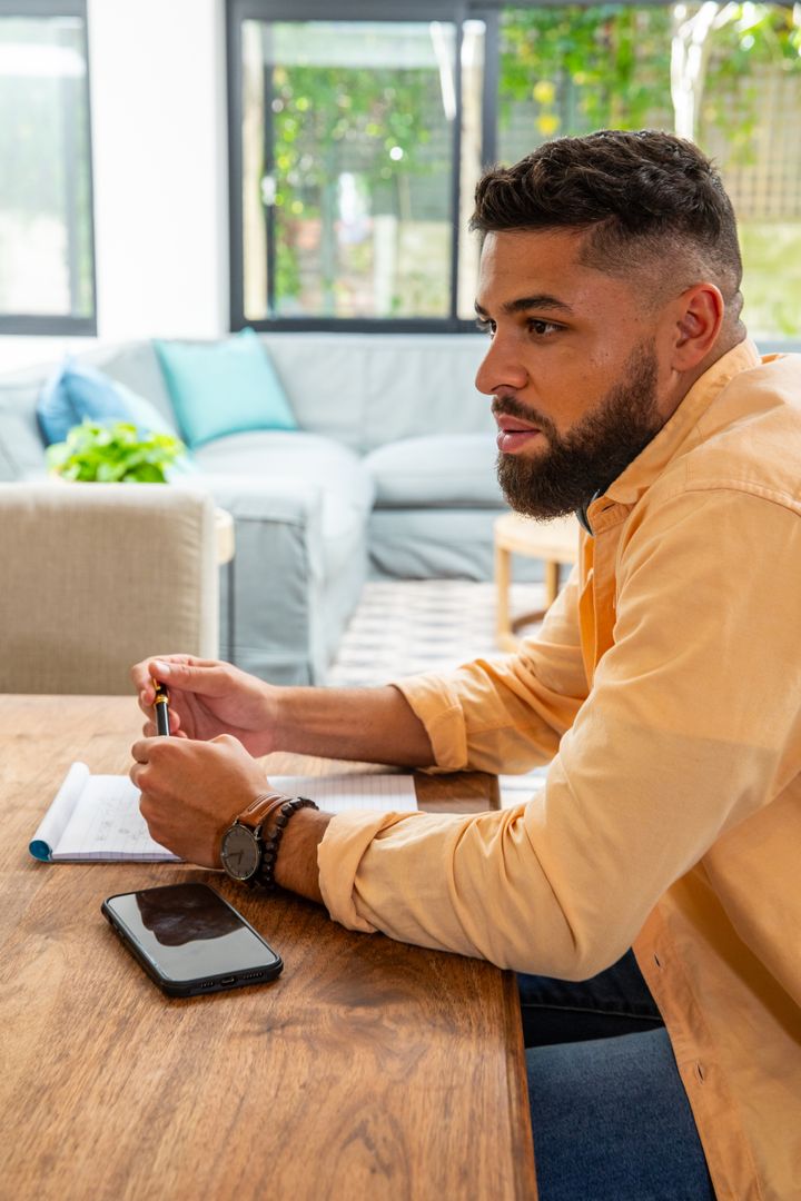 Man Reflecting at Home with Notepad and Smartphone