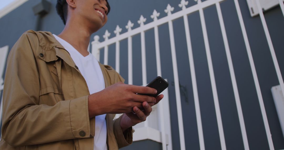 Young Man Smiling and Using Smartphone in Urban Setting - Free Images, Stock Photos and Pictures on Pikwizard.com