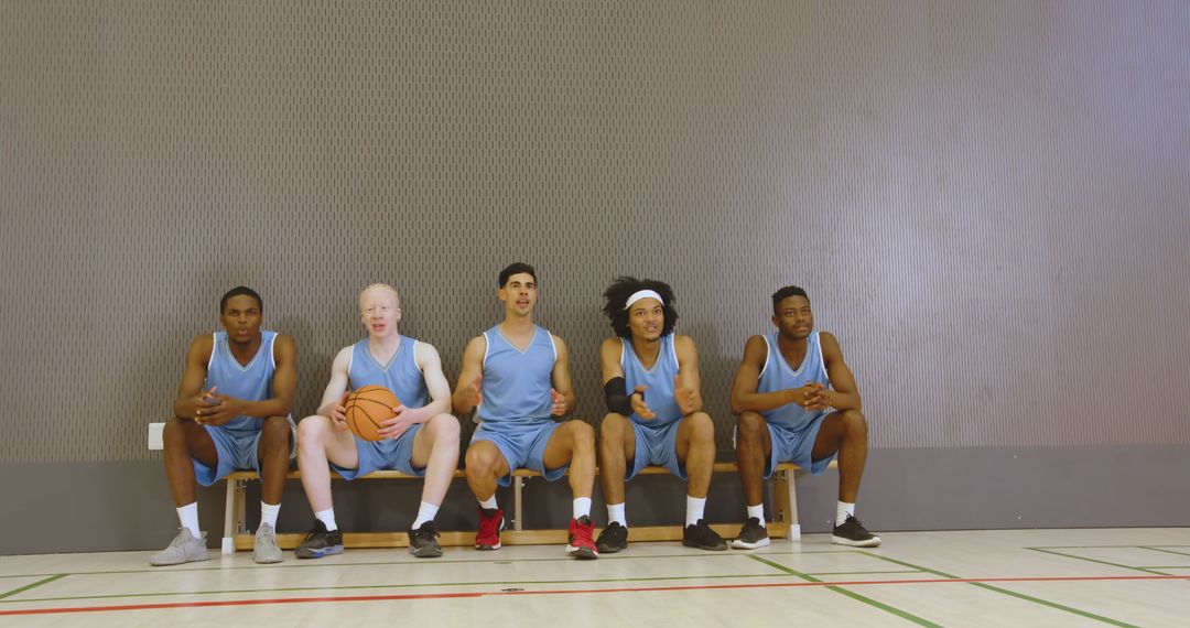 Diverse Basketball Team Sitting on Bench in Blue Uniforms with Ball