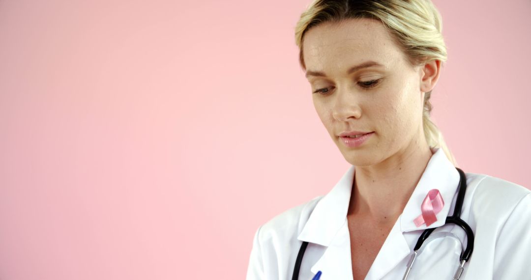 Thoughtful Doctor Wearing Pink Ribbon Against Pink Background - Free Images, Stock Photos and Pictures on Pikwizard.com