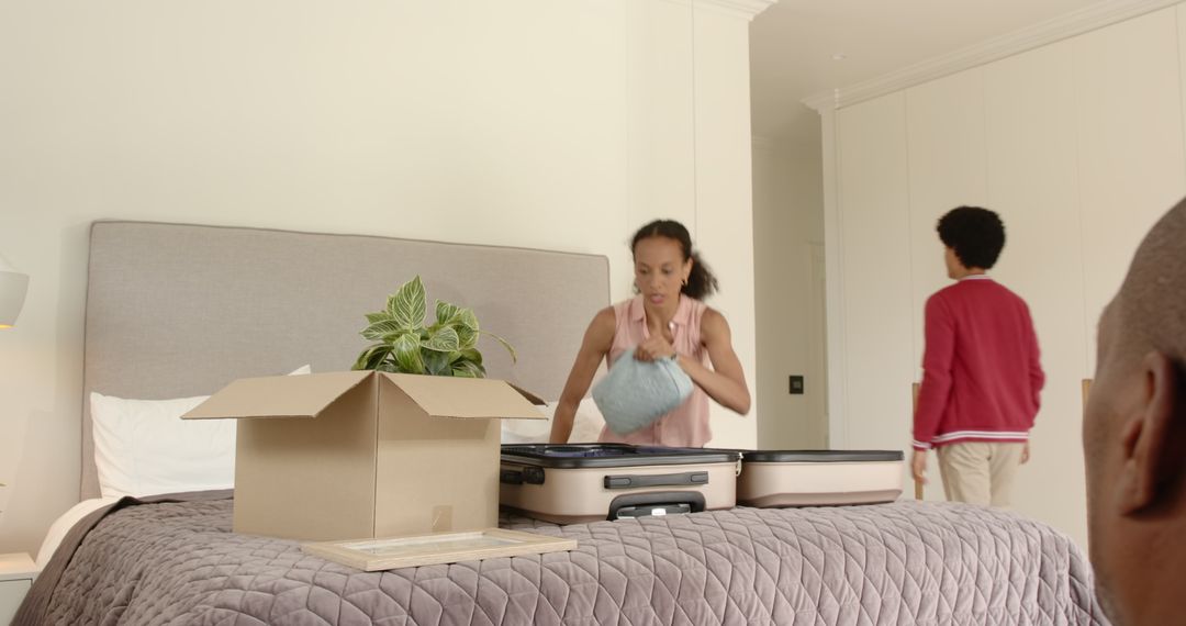 Woman Organizing Suitcase on Bed While Man Walking in Bedroom