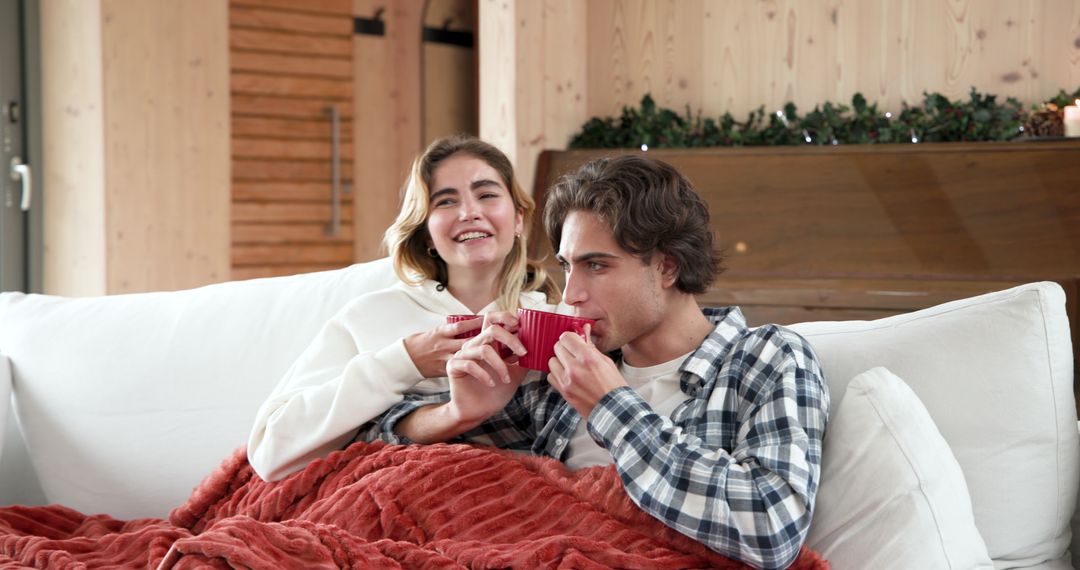 Couple Relaxing on Couch Under Festive Garland Lights with Red Blankets and Mugs