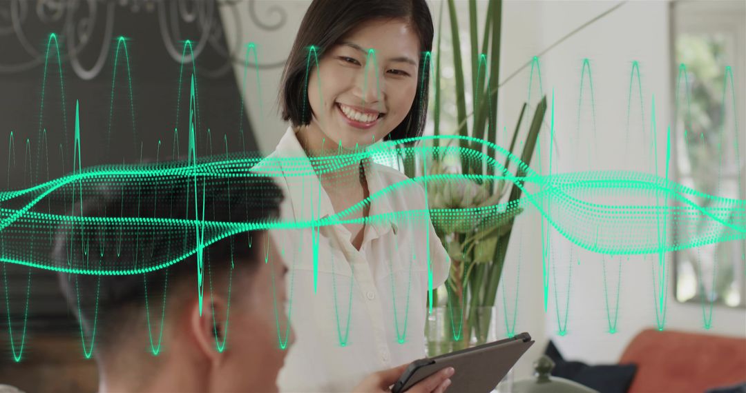 Smiling Asian woman presenting with tablet as team reviews green data-wave overlay for analytics