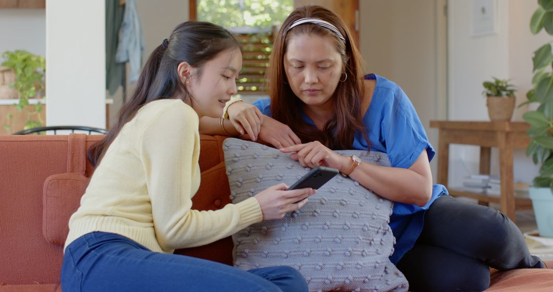 Asian Mother and Daughter Relaxing Together with Smartphone at Home