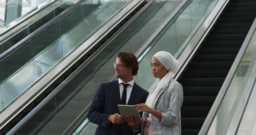 Businesswoman in Hijab Discussing with Colleague Holding Tablet Near Escalators - Free Images, Stock Photos and Pictures on Pikwizard.com