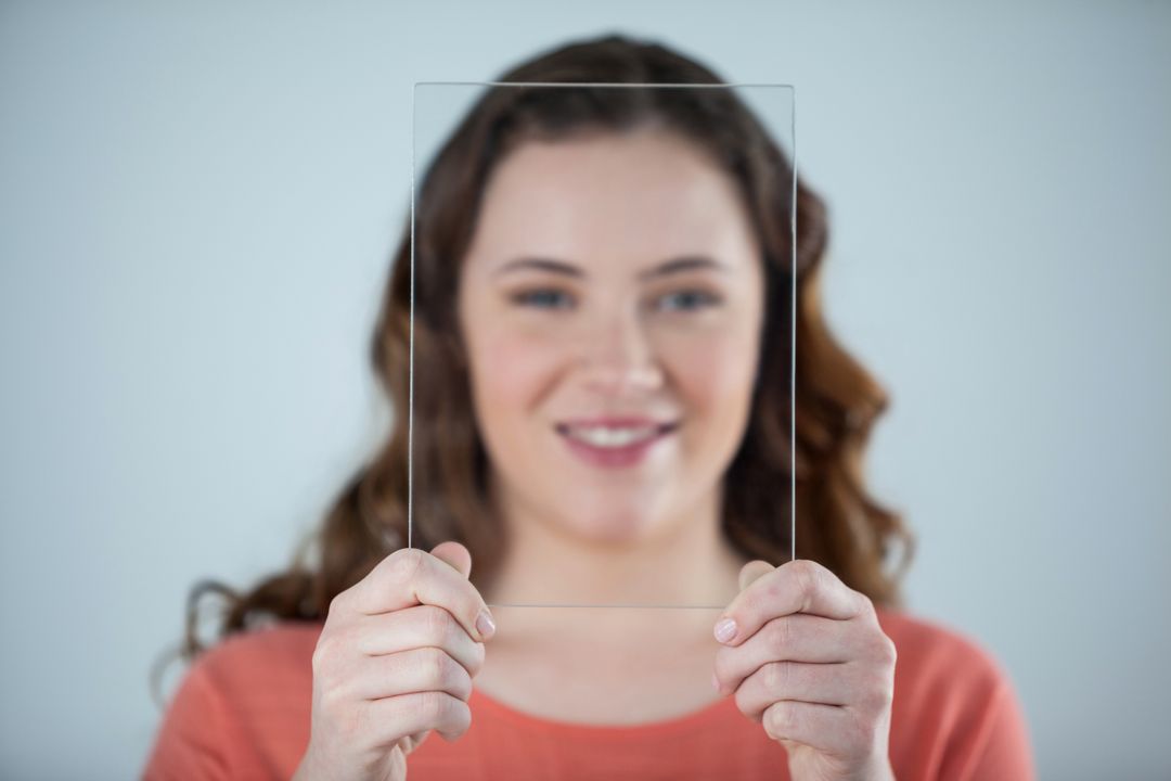Smiling Woman Holding Glass Sheet Against Face - Free Images, Stock Photos and Pictures on Pikwizard.com