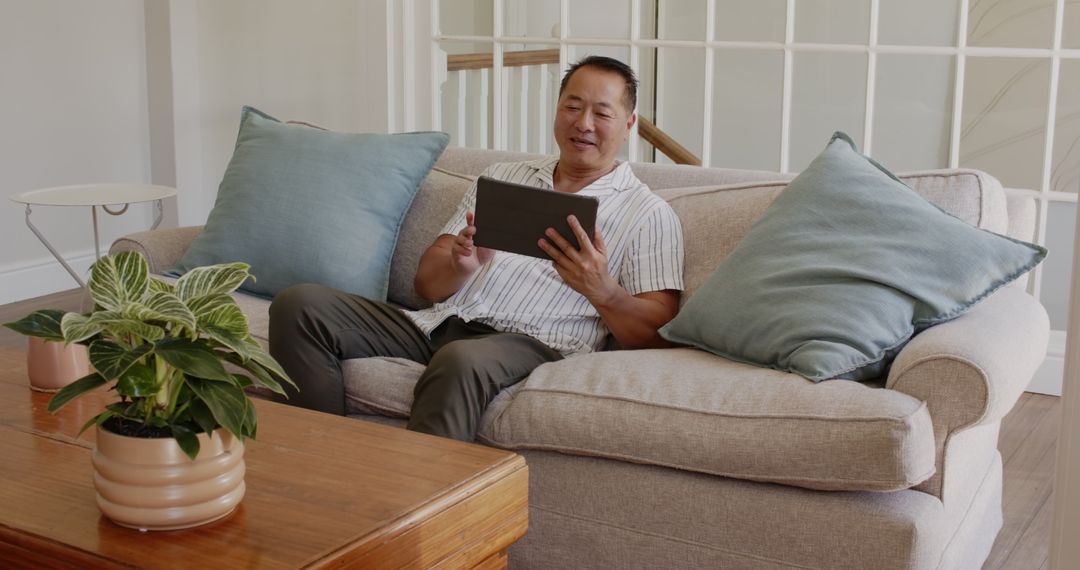 Asian Male Relaxing at Home with Tablet Technology