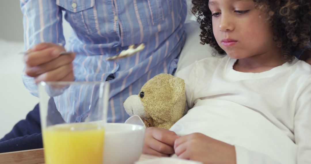 Mother taking care of ill child in bed with food and orange juice - Free Images, Stock Photos and Pictures on Pikwizard.com