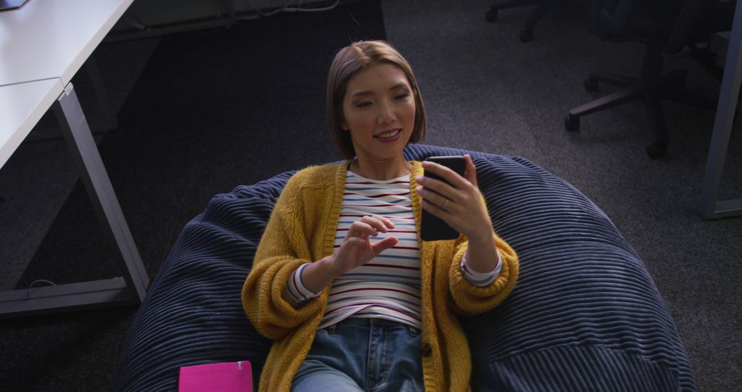 Smiling Woman Relaxing on Bean Bag Using Smartphone in Office - Free Images, Stock Photos and Pictures on Pikwizard.com