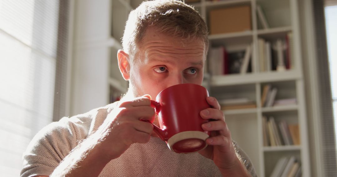 Man Drinking from Red Mug in Bright Room with Bookshelves - Free Images, Stock Photos and Pictures on Pikwizard.com