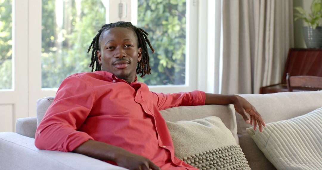 Smiling Young Black Man Relaxing on Couch at Home in Casual Red Shirt - Free Images, Stock Photos and Pictures on Pikwizard.com