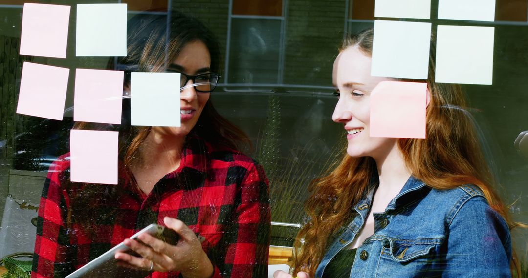 Two Women Collaborating on Project with Sticky Notes on Glass - Free Images, Stock Photos and Pictures on Pikwizard.com