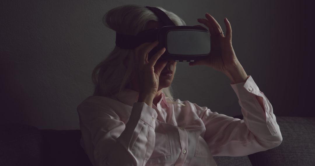 Elderly Woman Engages with Virtual Reality Headset in Dark Room - Free Images, Stock Photos and Pictures on Pikwizard.com