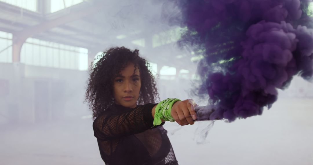 Confident African American Woman Holding Purple Smoke Bomb in Warehouse - Free Images, Stock Photos and Pictures on Pikwizard.com