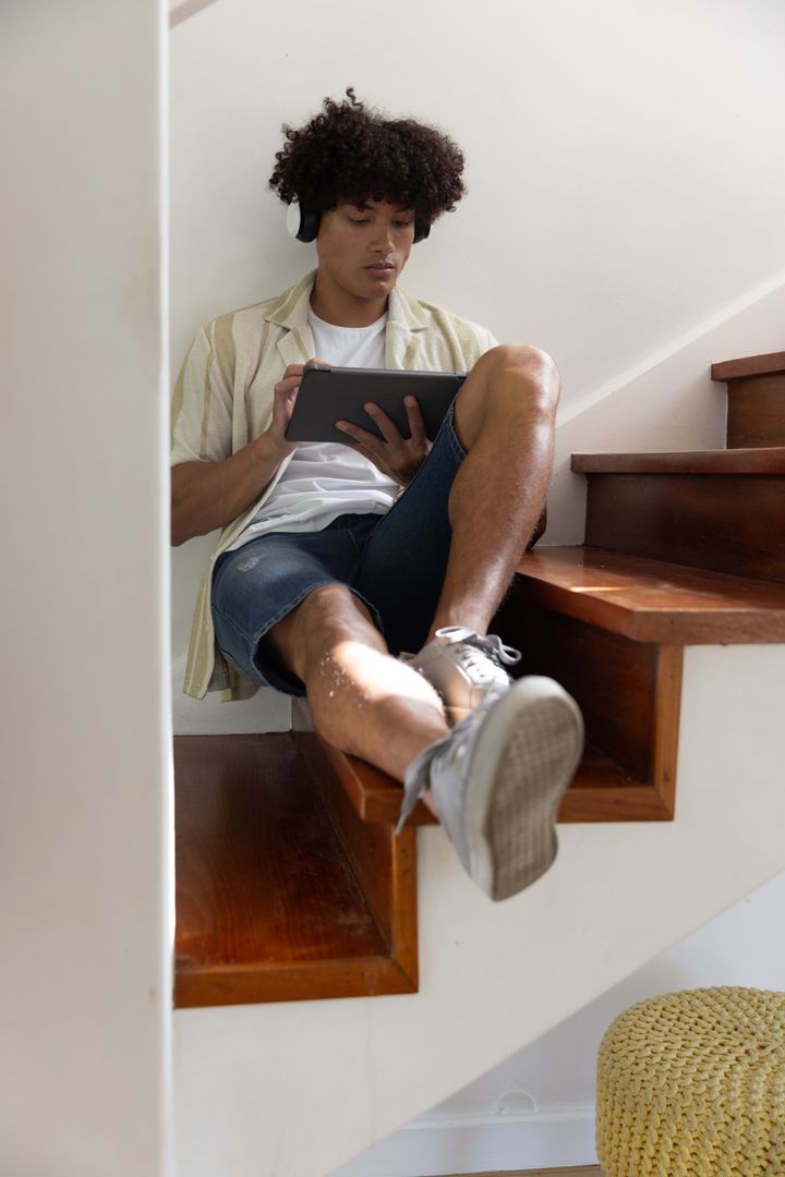 Man Relaxing on Stairs with Tablet and Headphones at Home