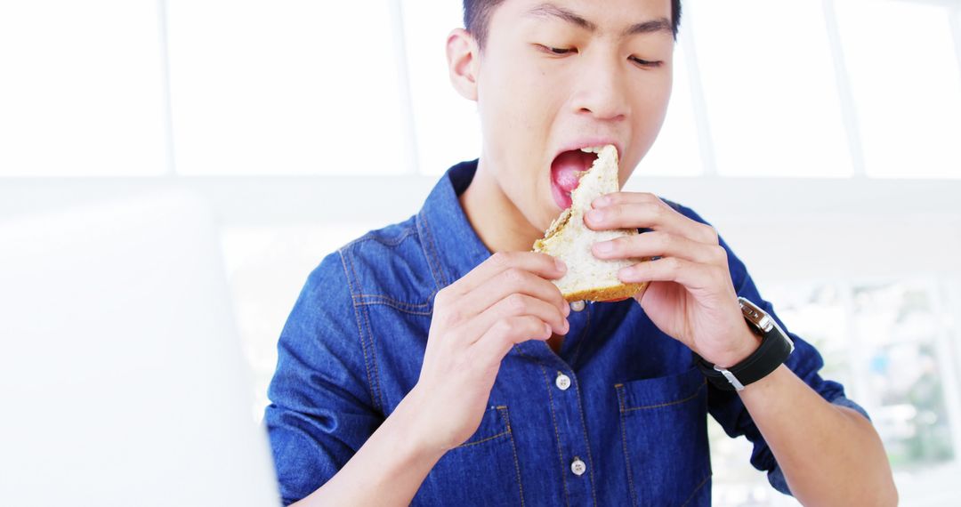 Young Man Eating Sandwich in Bright Office Environment - Free Images, Stock Photos and Pictures on Pikwizard.com