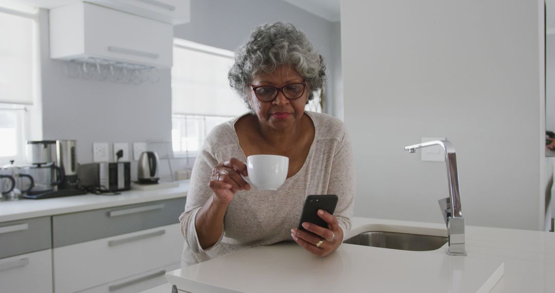 Senior Woman Drinking Coffee and Using Smartphone in Modern Kitchen - Free Images, Stock Photos and Pictures on Pikwizard.com