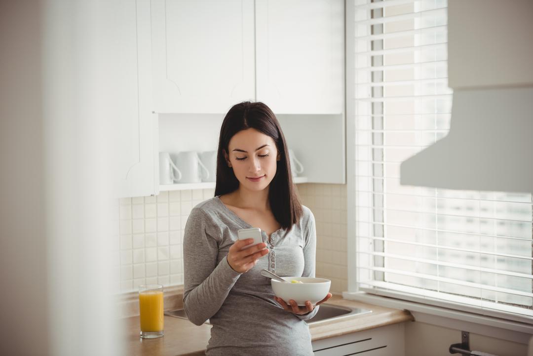 Woman Using Smartphone While Holding Bowl in Kitchen - Free Images, Stock Photos and Pictures on Pikwizard.com