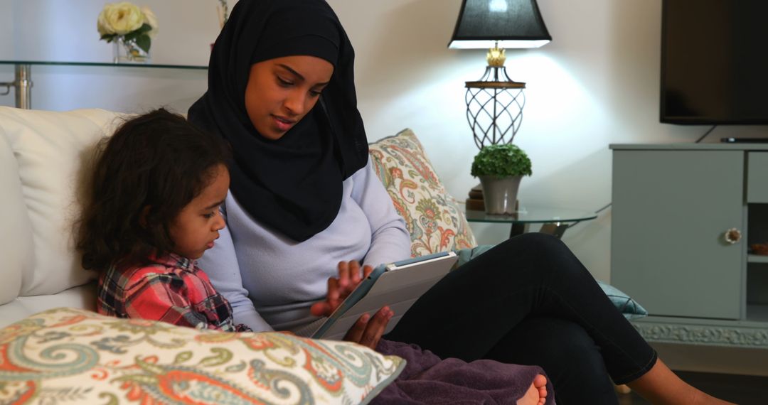 Hijabi Mother and Daughter Bonding on Sofa with Tablet