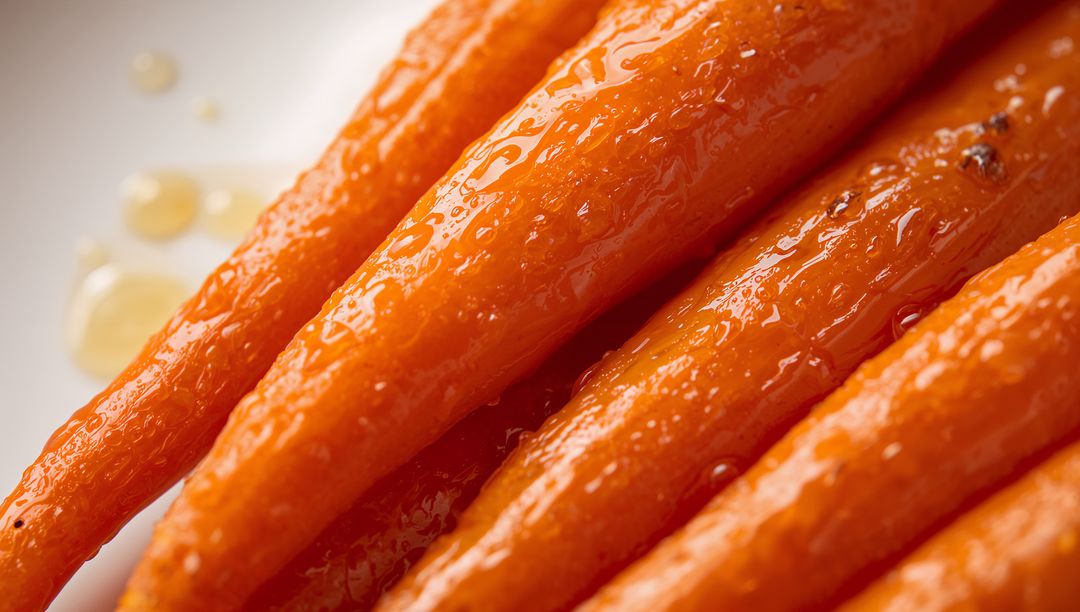 Glistening glazed baby carrots gleaming with honey drizzle on white plate close-up macro