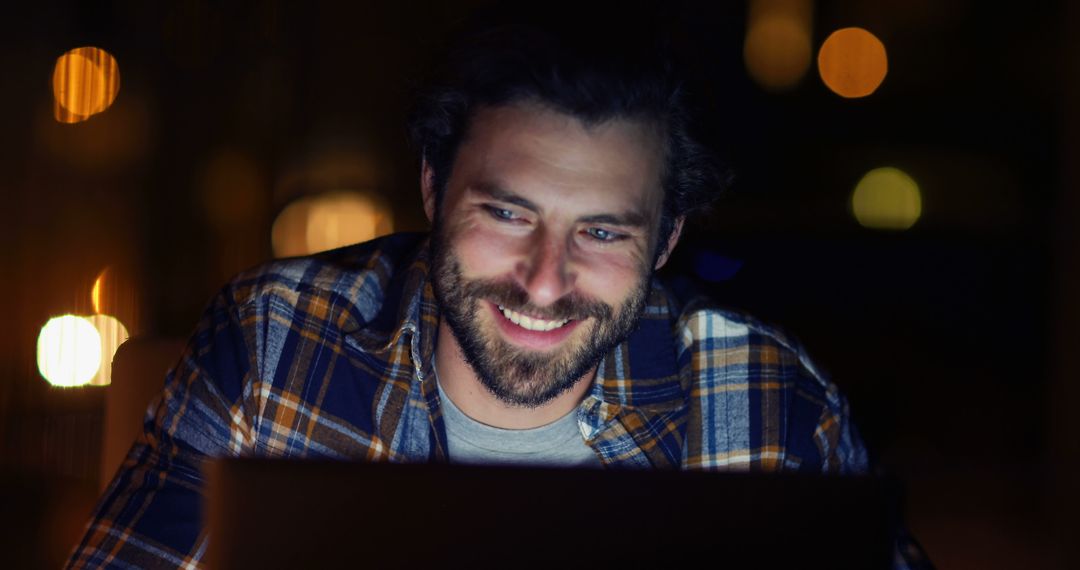 Man Smiling Working on Laptop at Night Under Warm Lighting - Free Images, Stock Photos and Pictures on Pikwizard.com