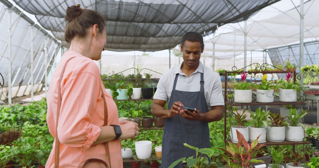Nursery Worker Assisting Customer in Lush Greenhouse