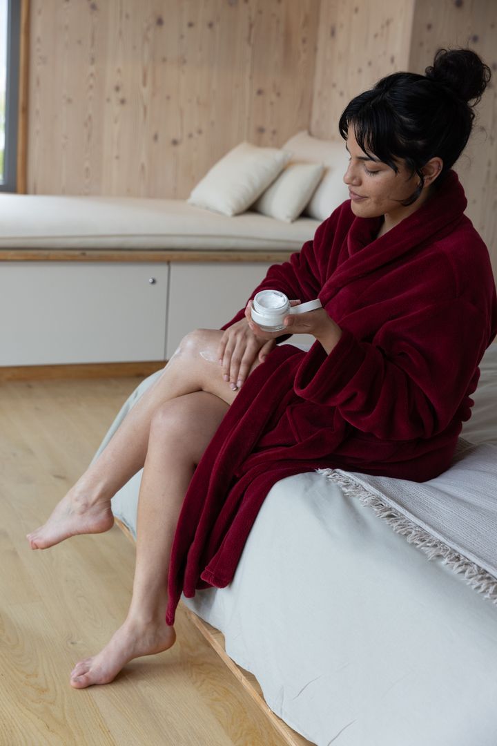 Hispanic Woman in Red Robe Applying Cream for Self-Care and Relaxation