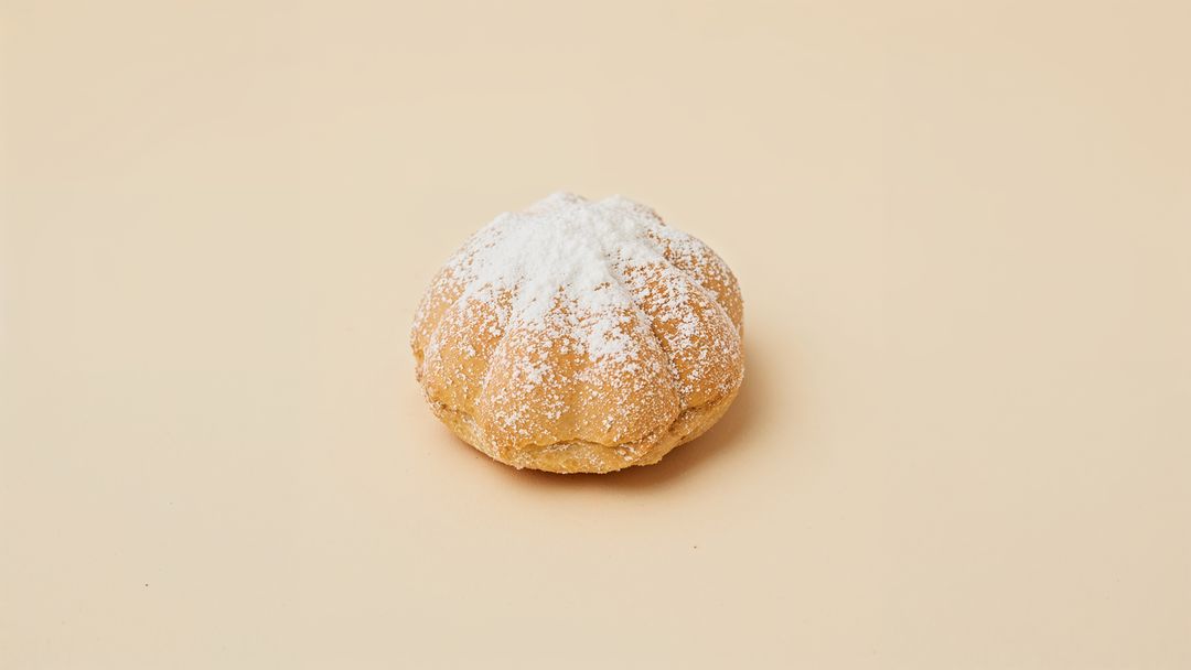 Pumpkin-Shaped Gourmet Pastry with Powdered Sugar on Beige Surface